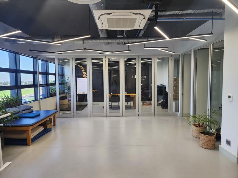 Modern office space featuring exposed ceilings, linear lighting, cassette air conditioning, and large glass folding doors providing natural light and flexible room division.