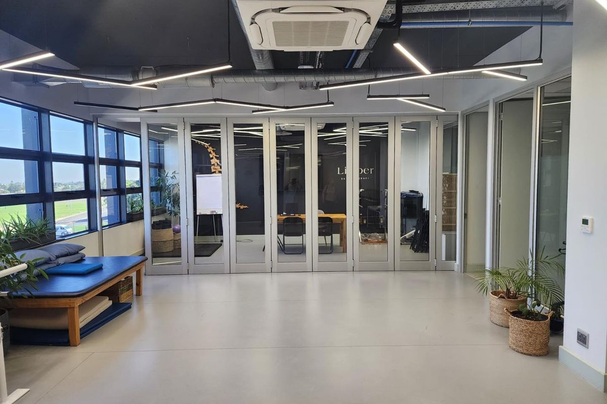 Modern office space featuring exposed ceilings, linear lighting, cassette air conditioning, and large glass folding doors providing natural light and flexible room division.