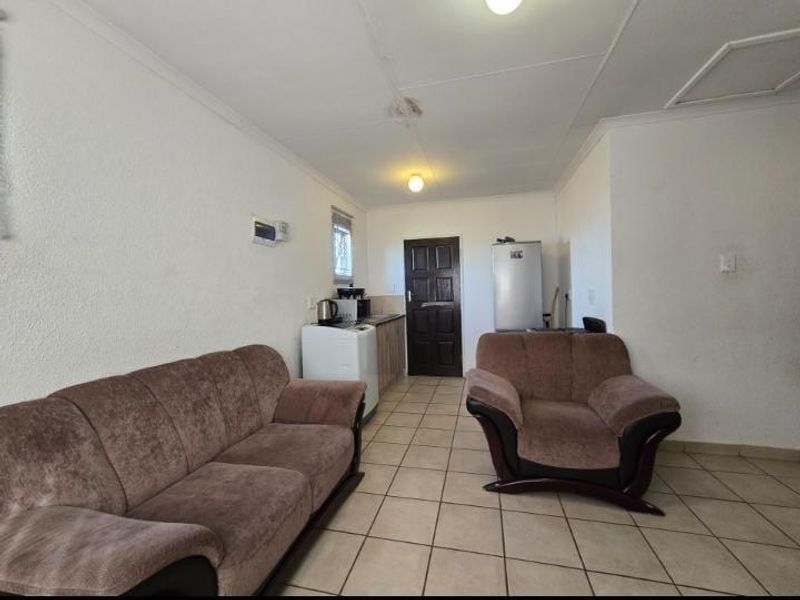 Open plan living area featuring tiled flooring and a compact kitchen corner, showing signs of ceiling water damage.