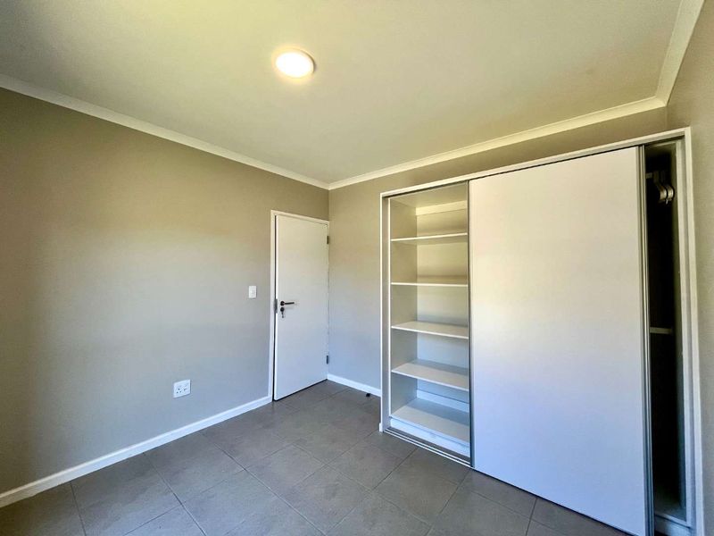 A clean, empty bedroom featuring neutral wall tones, tiled flooring, and a large built-in sliding door wardrobe with integrated shelving.