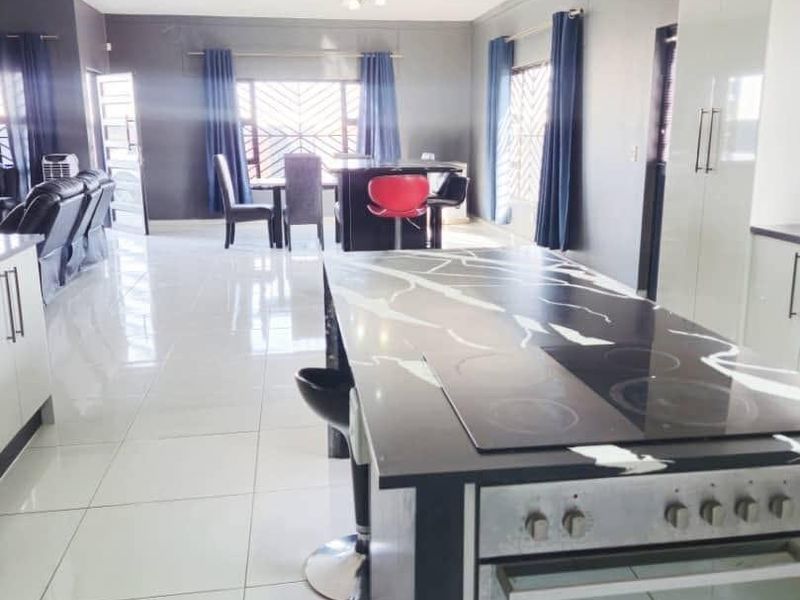 Spacious open-plan living area featuring a modern kitchen with a central island, built-in oven, hob, and sleek tiled flooring throughout.