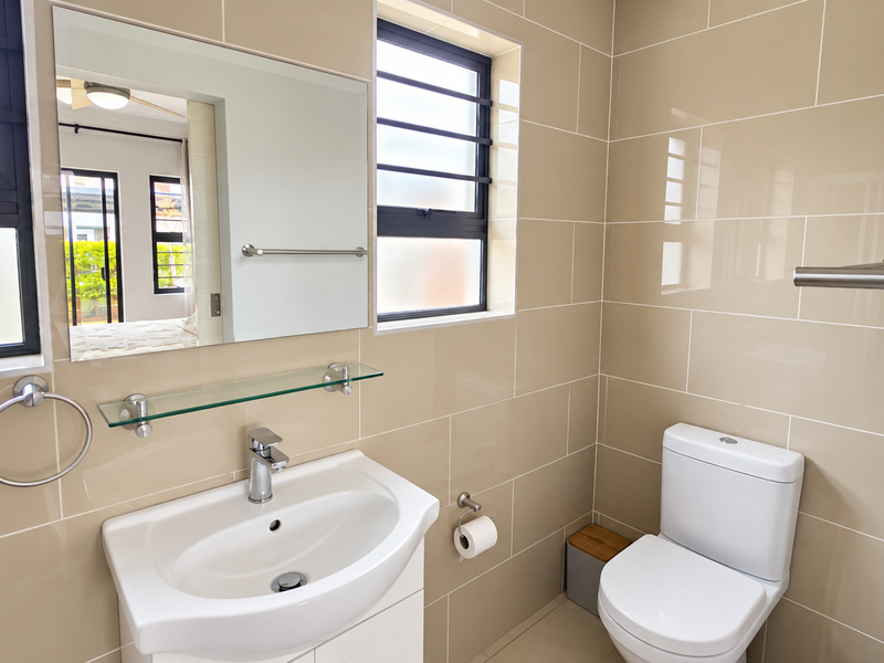 A modern, well-maintained bathroom featuring neutral ceramic wall tiles, a vanity basin with chrome fixtures, and a wall-mounted mirror.