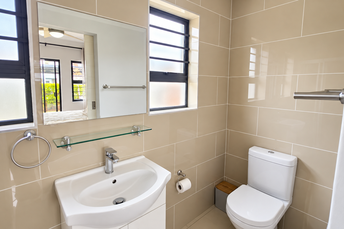 A modern, well-maintained bathroom featuring neutral ceramic wall tiles, a vanity basin with chrome fixtures, and a wall-mounted mirror.