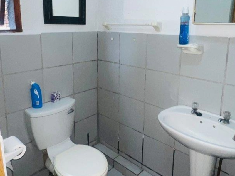 A functional bathroom featuring a pedestal basin, toilet, and tiled wall finishes, currently showing signs of wear and dated aesthetics.