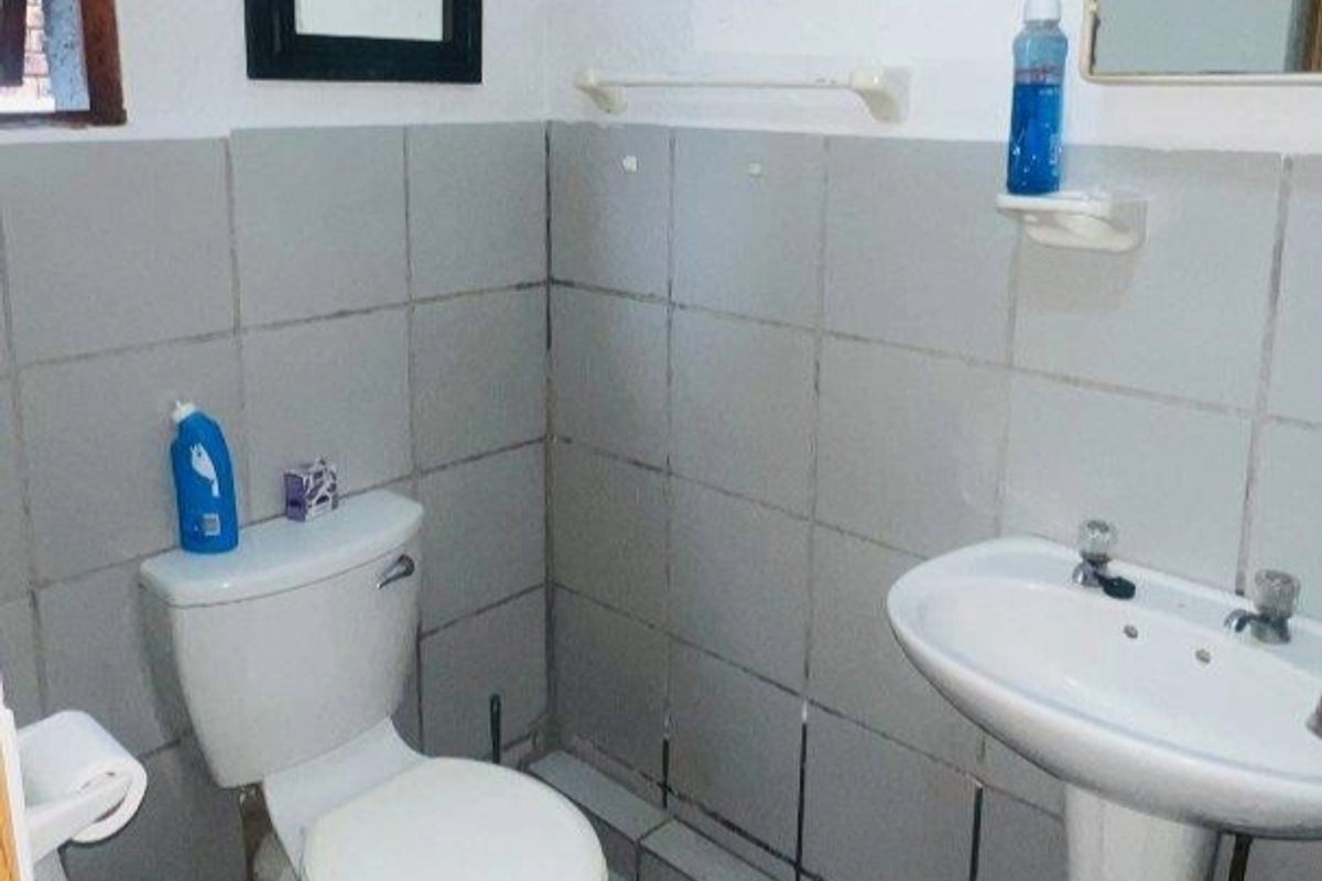 A functional bathroom featuring a pedestal basin, toilet, and tiled wall finishes, currently showing signs of wear and dated aesthetics.