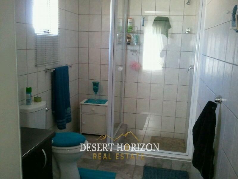 A functional bathroom featuring a glass-enclosed shower, tiled walls, and standard toilet fixtures.