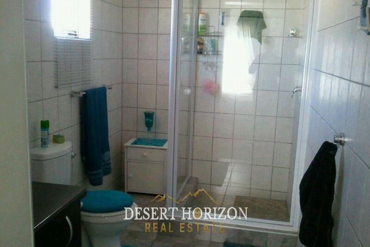 A functional bathroom featuring a glass-enclosed shower, tiled walls, and standard toilet fixtures.