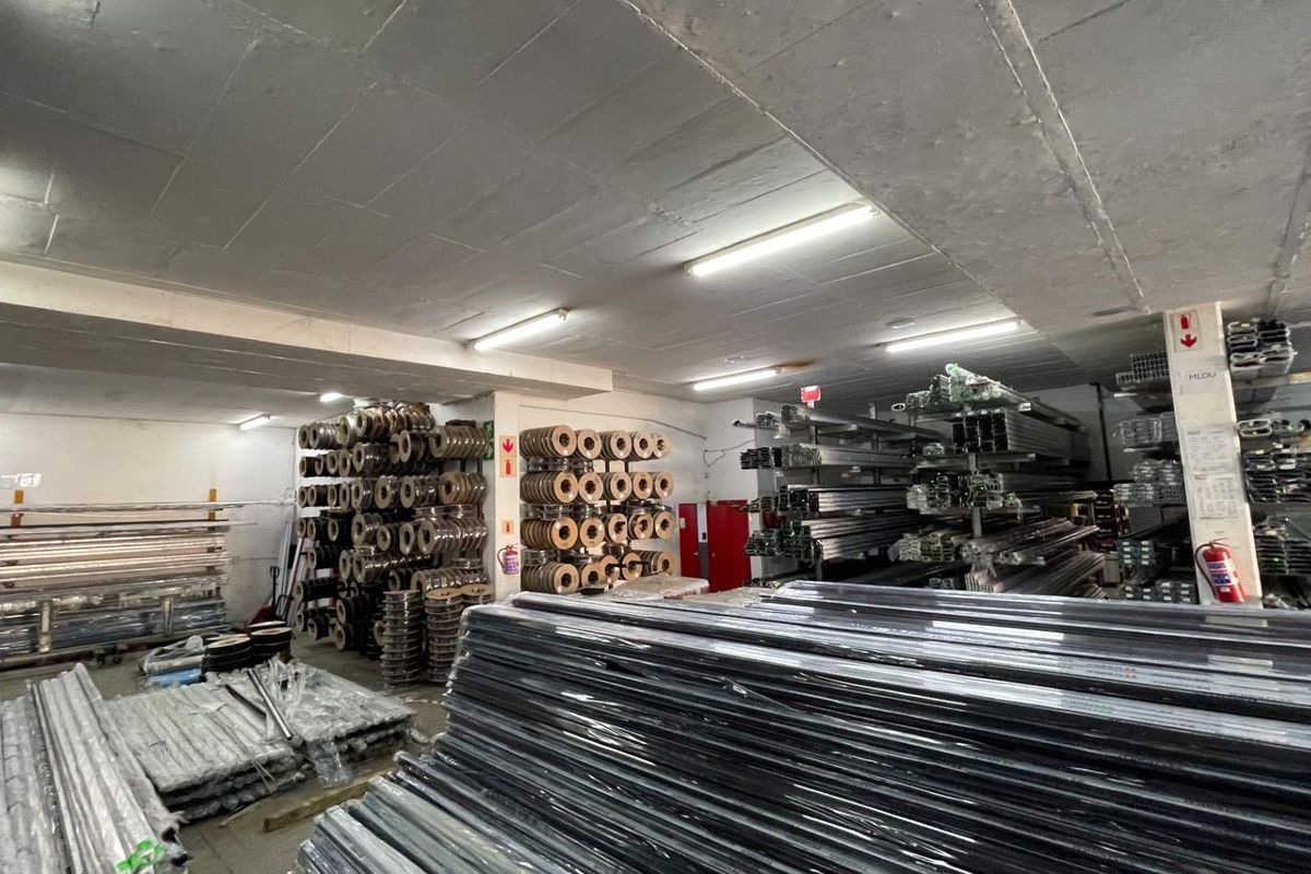 A functional industrial utility or storage space featuring concrete ceilings, overhead fluorescent lighting, and extensive metal racking systems for inventory management.