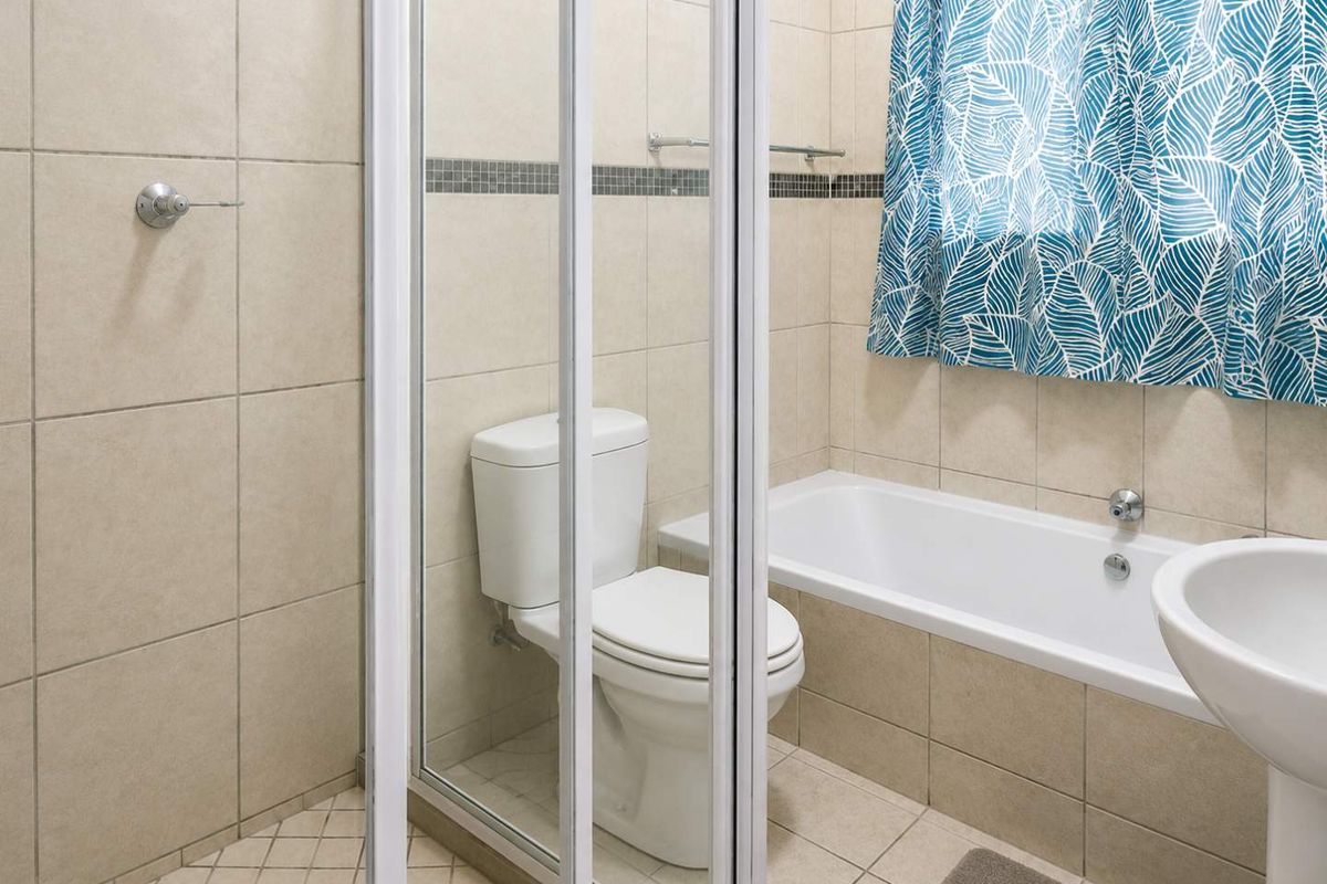 A functional bathroom featuring a shower enclosure, bathtub, pedestal basin, and toilet with neutral wall and floor tiling.