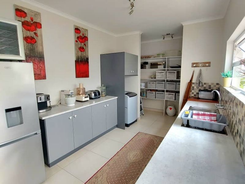 A functional scullery area featuring grey cabinetry, tiled flooring, a stainless steel sink, and an adjoining walk-in pantry space.