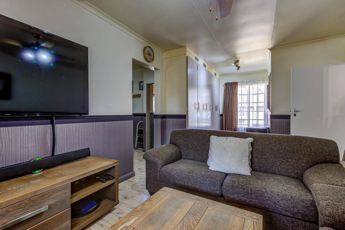 A living room featuring wainscoting, built-in storage cupboards, tiled flooring, and a ceiling fan, offering a functional and well-maintained living space.