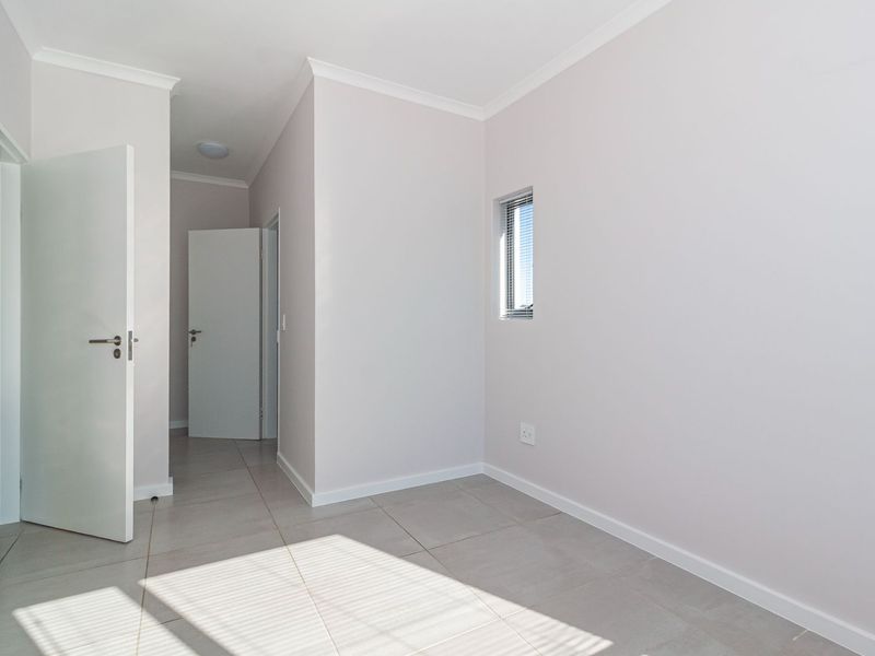 A bright, empty bedroom featuring neutral tiled flooring, clean walls, and modern internal doors, offering a blank canvas for personalization.