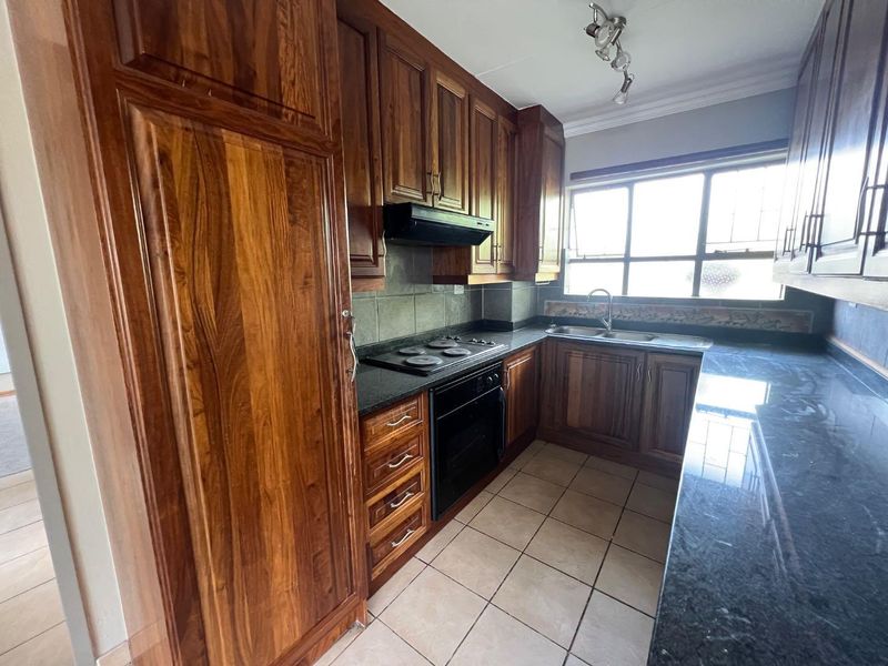 A functional kitchen featuring warm-toned wooden cabinetry, granite countertops, a built-in oven with hob, and tiled flooring.
