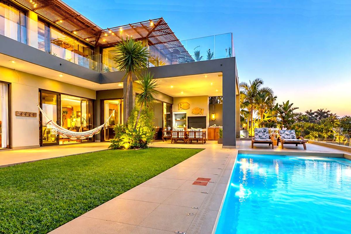 A luxurious rear exterior featuring a modern swimming pool, expansive covered patio with timber pergola, and seamless indoor-outdoor flow through large sliding glass doors.