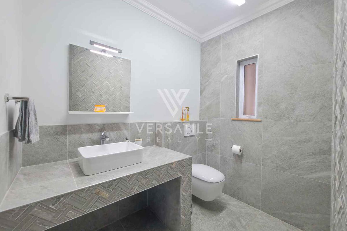 Modern bathroom featuring a floating vanity with a vessel sink, wall-mounted mirror, and floor-to-ceiling grey stone-look tiling.