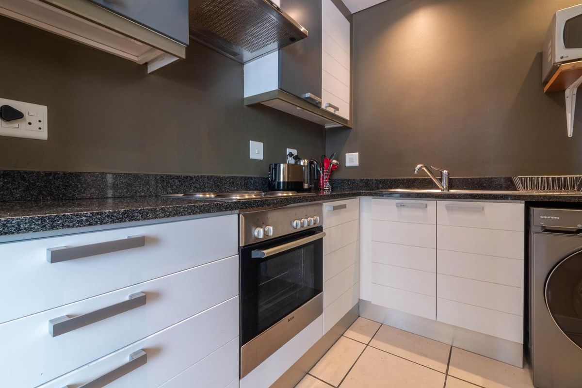 A compact, modern kitchen featuring granite countertops, built-in cabinetry, a stainless steel oven, and an integrated extractor fan with tiled flooring.