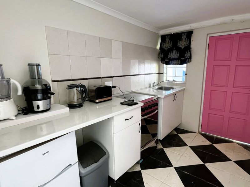 Compact kitchen featuring white cabinetry, tiled splashback, stainless steel sink, and a distinctive checkerboard floor pattern with direct exterior access.