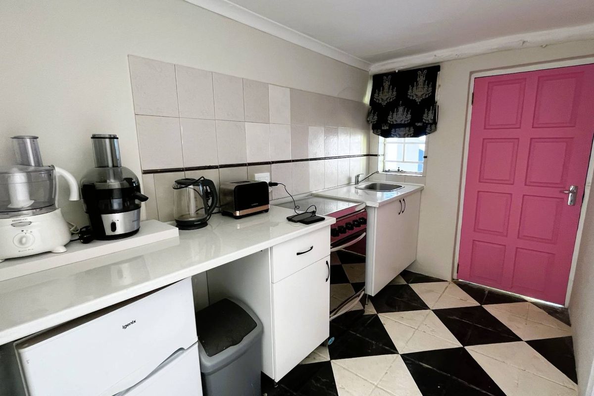 Compact kitchen featuring white cabinetry, tiled splashback, stainless steel sink, and a distinctive checkerboard floor pattern with direct exterior access.