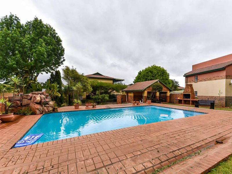 Outdoor pool area featuring brick paving, a built-in braai, and a decorative rock feature, set within a communal townhouse garden space.