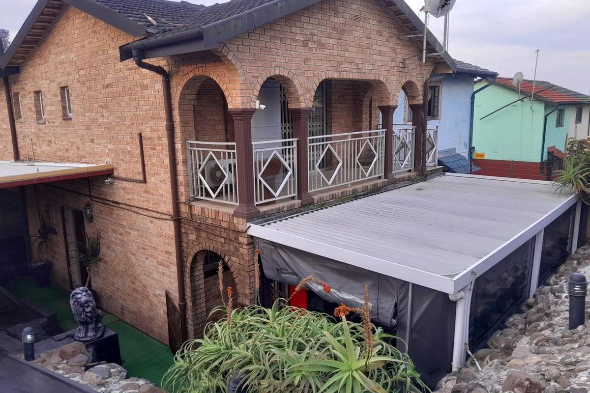 Two-story face brick residence featuring an upper-level balcony with arched detailing and a lower-level covered patio area with an integrated awning.