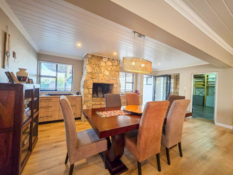 Spacious dining area featuring a prominent stone fireplace, timber-look flooring, and a tongue and groove ceiling with modern pendant lighting.