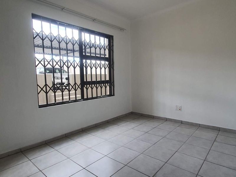 An empty bedroom featuring neutral tiled flooring and a window fitted with a security gate.