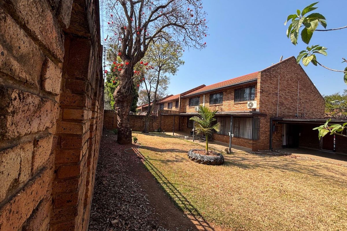 Rear view of a face brick townhouse featuring a private garden, covered patio area, and established trees.