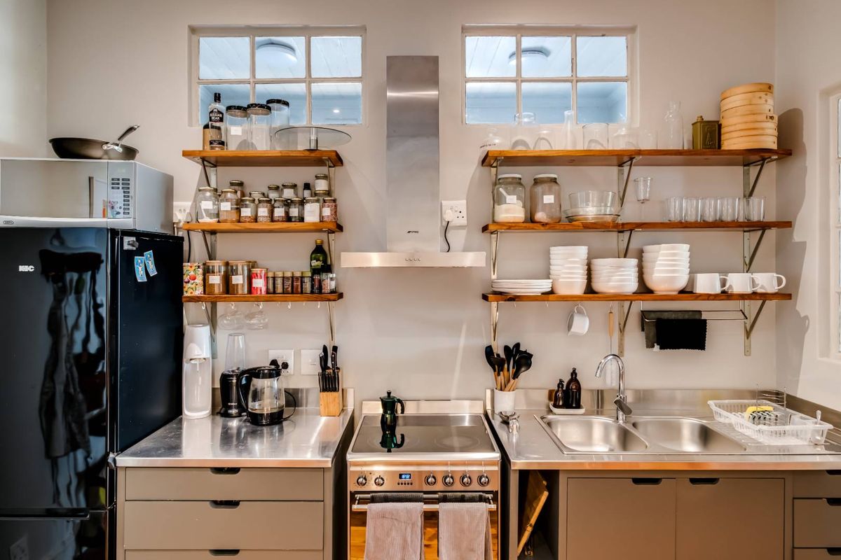 A functional kitchen featuring stainless steel countertops, a built-in oven with extractor fan, double sink, and open timber shelving for storage.