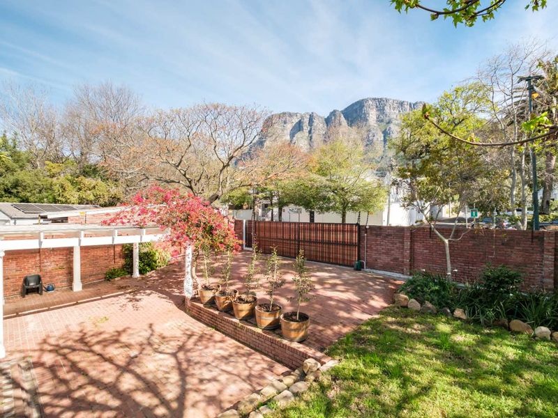 A spacious rear courtyard featuring brick paving, a pergola, and a brick boundary wall, set against a scenic mountain backdrop.