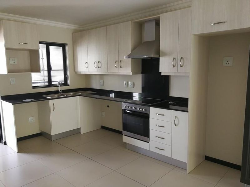 Modern kitchen featuring light wood-finish cabinetry, dark granite countertops, integrated stainless steel oven, hob, and extractor fan with tiled flooring.