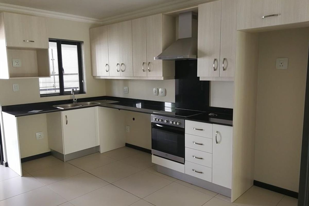 Modern kitchen featuring light wood-finish cabinetry, dark granite countertops, integrated stainless steel oven, hob, and extractor fan with tiled flooring.