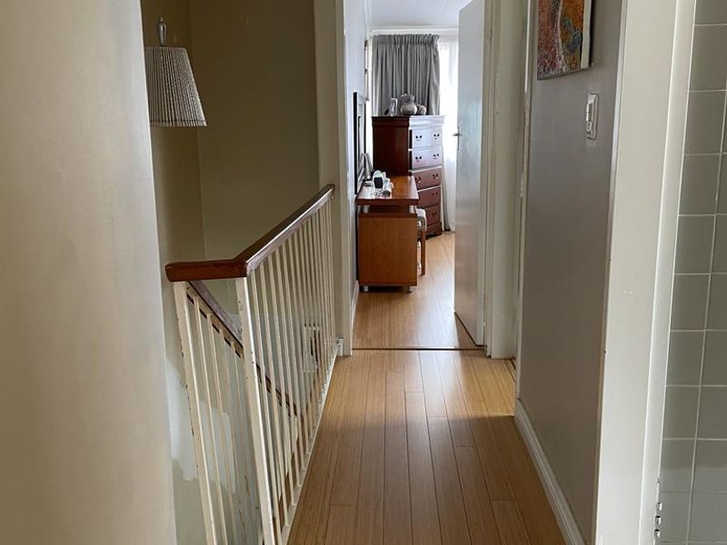 A functional upper-level hallway featuring laminate flooring and a staircase balustrade, leading towards a bedroom area.