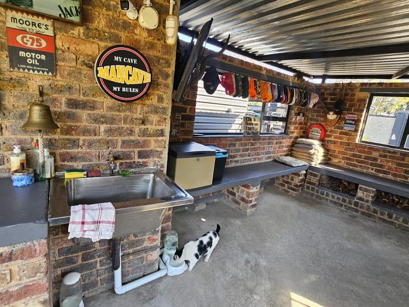 Covered outdoor patio area featuring exposed brick walls, a stainless steel sink, concrete countertops, and built-in brick seating, ideal for an entertainment space.