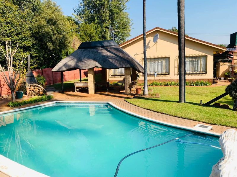 Rear garden featuring a swimming pool, brick-paved surround, and a traditional thatch lapa entertainment area.