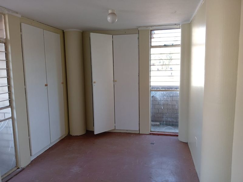 An empty bedroom featuring built-in cupboards, structural columns, and louvered windows, offering a blank canvas for renovation and interior design updates.