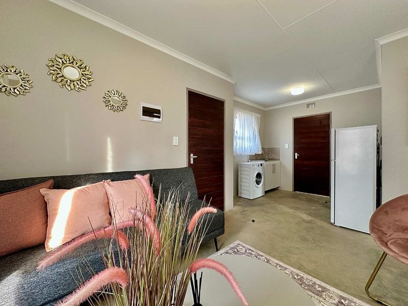 Open plan living area featuring a compact kitchenette with built-in cabinetry and sink, finished with neutral walls and solid core doors.
