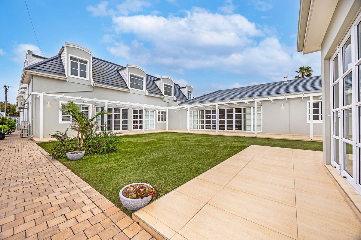 A well-maintained rear exterior featuring a paved patio, pergola, artificial lawn, and multiple sets of french doors leading into the home.