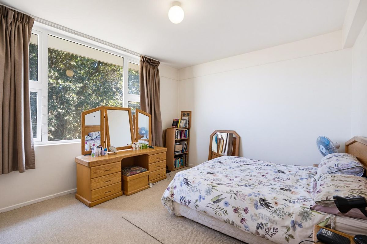 A well-lit bedroom featuring neutral carpeting, a large window providing natural light, and a simple, functional layout.