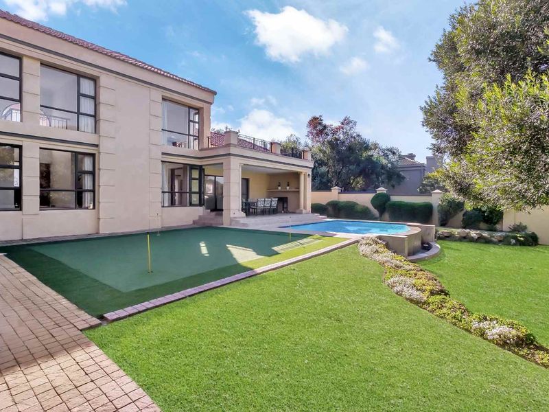Rear exterior view featuring a swimming pool, a private putting green, a covered patio area, and a well-maintained landscaped garden.