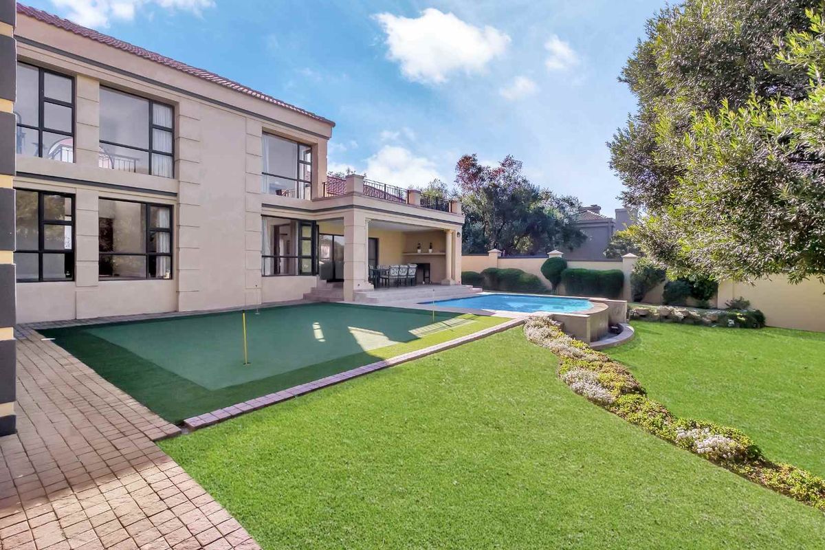 Rear exterior view featuring a swimming pool, a private putting green, a covered patio area, and a well-maintained landscaped garden.