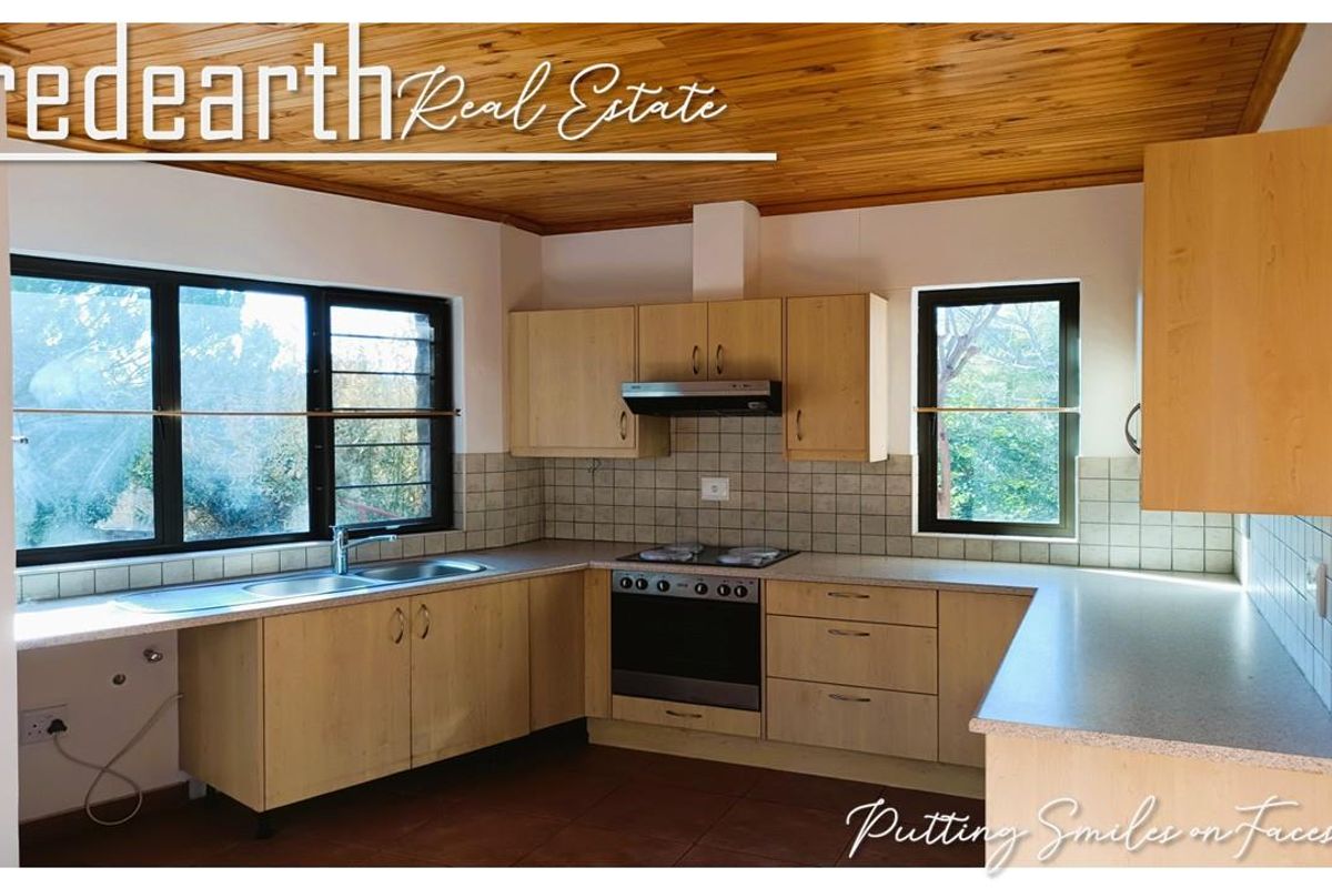 A functional kitchen featuring light wood cabinetry, built-in oven with hob, extractor fan, double sink, and a distinctive timber-paneled ceiling.