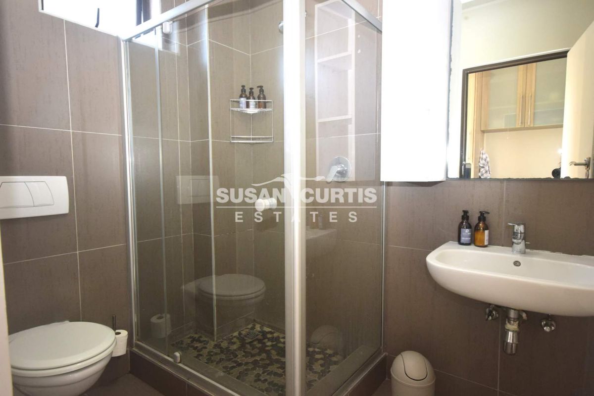 A modern bathroom featuring a glass shower enclosure, wall-mounted toilet, and a wall-hung basin with tiled finishes throughout.