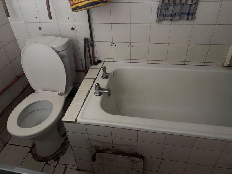 A dated bathroom featuring a standard toilet and bathtub with tiled finishes, currently requiring significant maintenance and renovation to improve its condition.