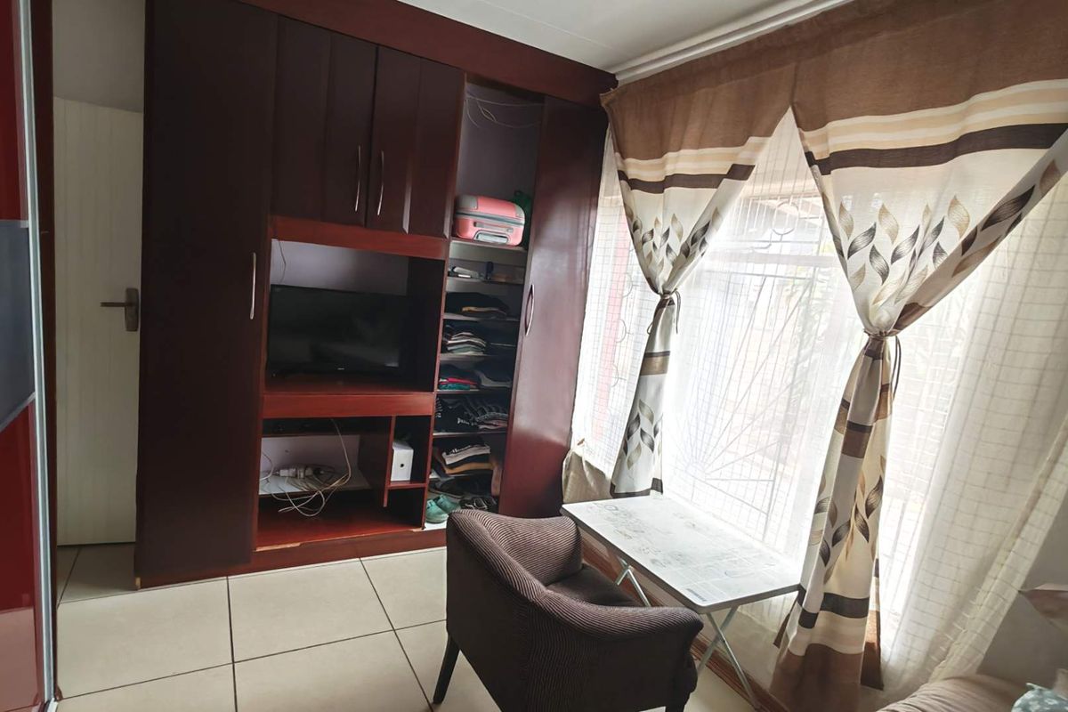 A bedroom featuring built-in dark wood cabinetry with integrated shelving and tiled flooring, illuminated by natural light through a window with security bars.