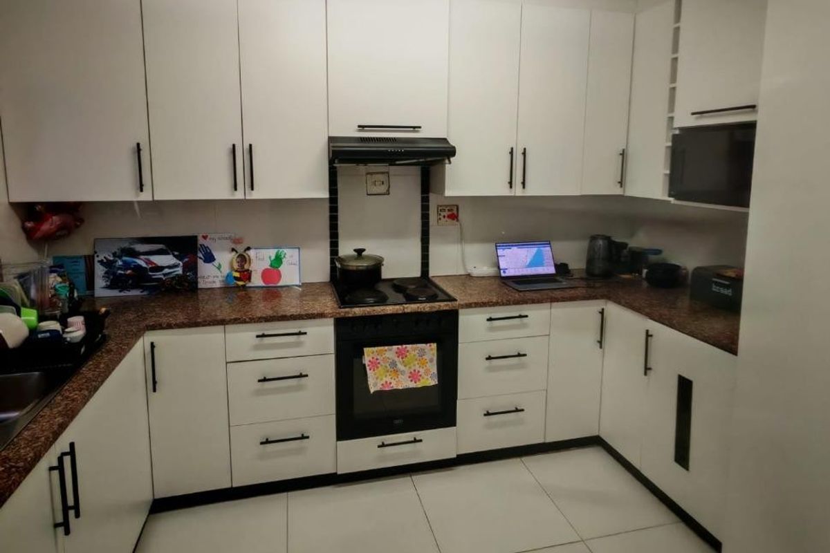 A functional U-shaped kitchen featuring white cabinetry, granite countertops, built-in oven, hob, and extractor fan with tiled flooring.