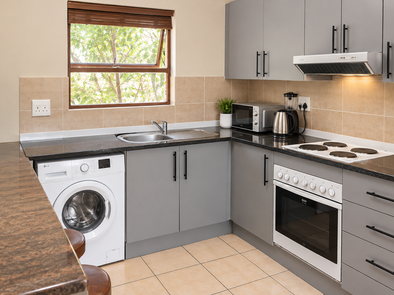 Modern kitchen featuring grey cabinetry, granite countertops, tiled backsplash, built-in oven, electric hob, extractor fan, and an integrated washing machine.