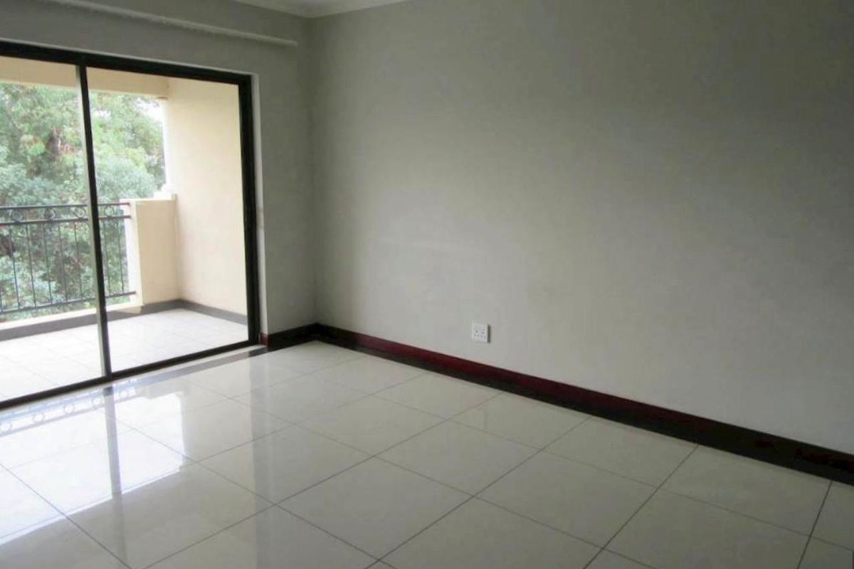 An empty living room featuring neutral tiled flooring, dark skirting boards, and a large sliding glass door providing access to an outdoor balcony.
