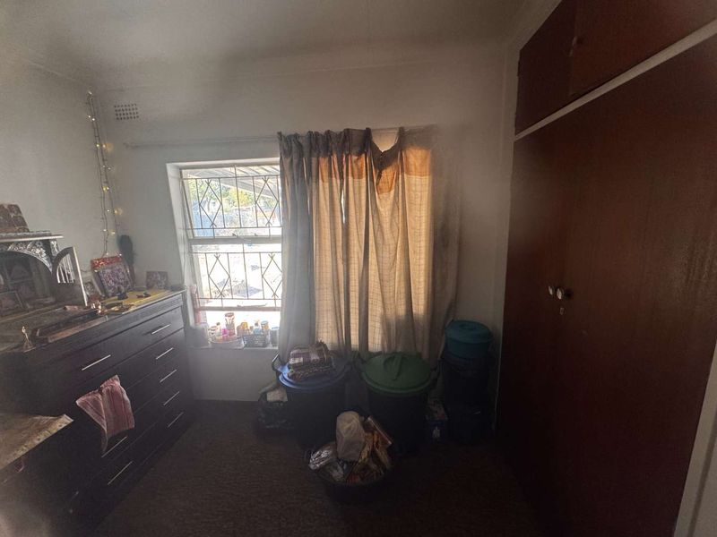 A bedroom featuring a built-in wardrobe, security bars on the window, and dated finishes, offering potential for modernization and improved layout.