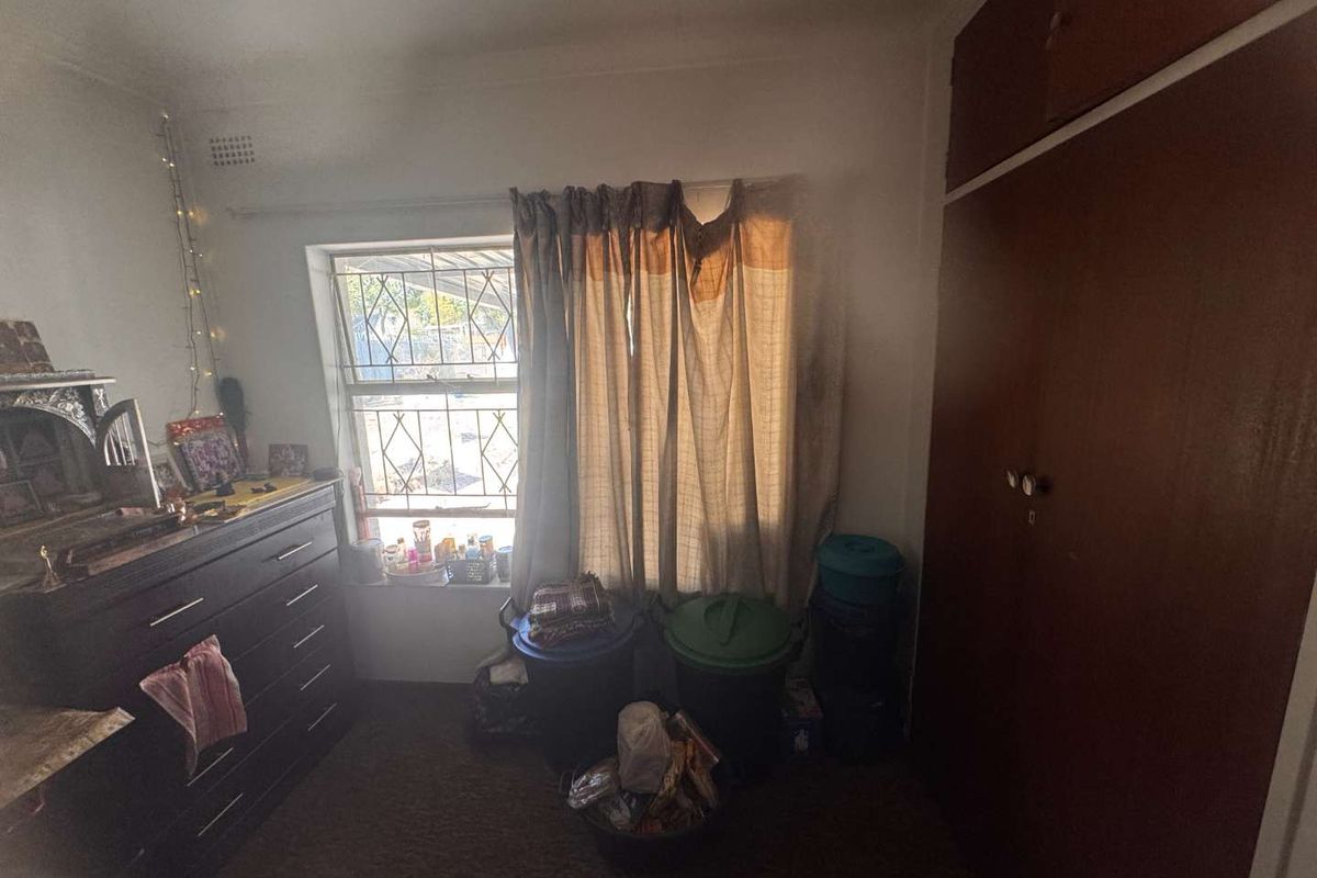 A bedroom featuring a built-in wardrobe, security bars on the window, and dated finishes, offering potential for modernization and improved layout.