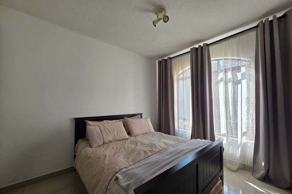 A bedroom featuring tiled flooring, a ceiling-mounted spotlight fixture, and a large window with an arched top allowing natural light.